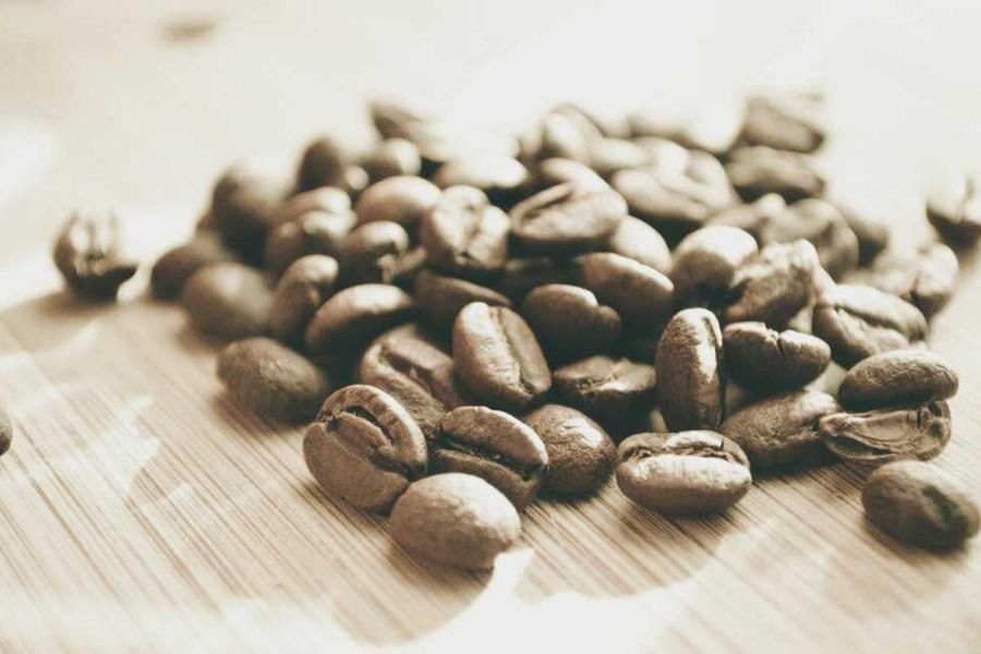 Roasted beans spread on a pale wooden board, soft focus behind