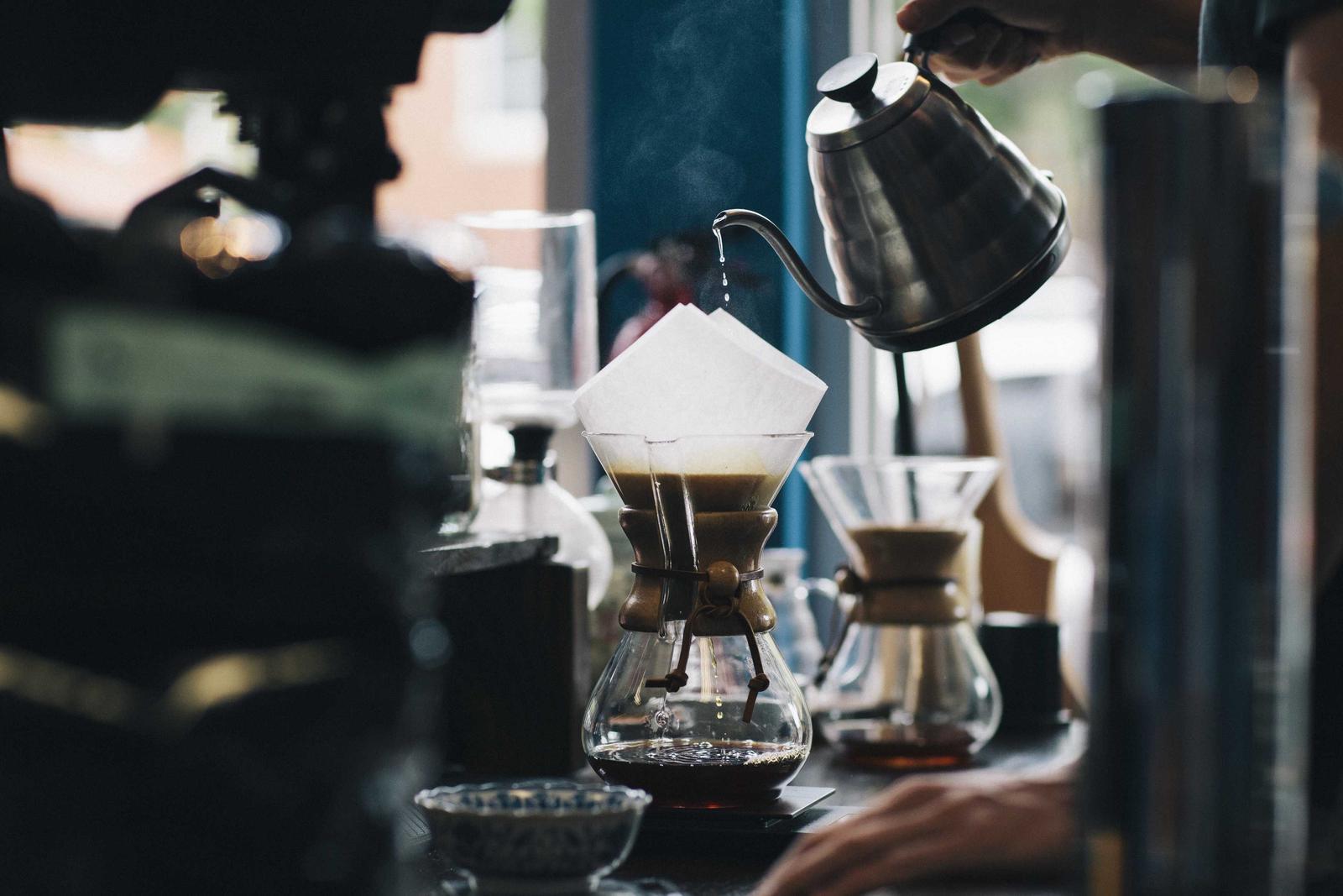 A gooseneck kettle pouring over a paper filter in a Chemex on a cafe counter